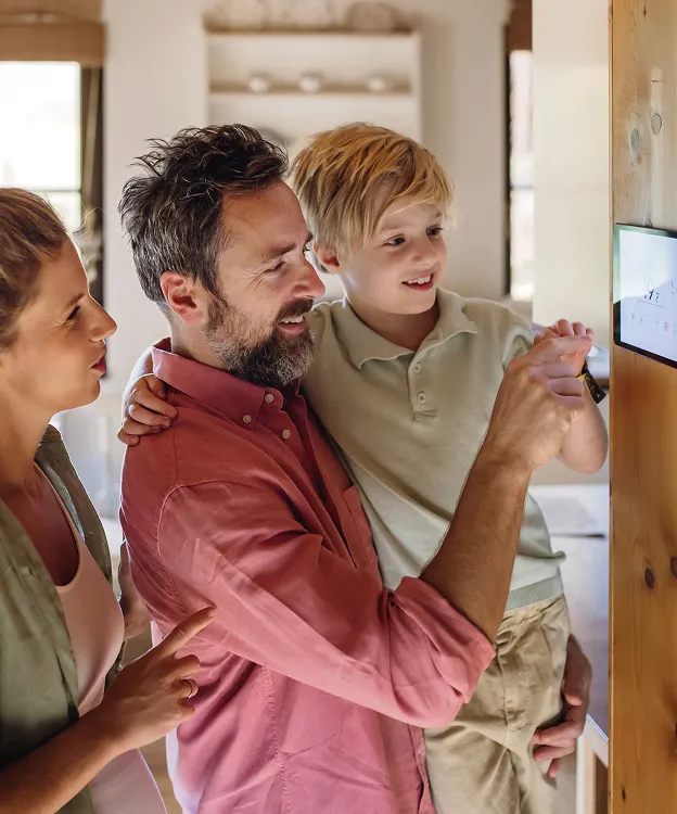 Famille souriante interagissant avec une tablette murale à la maison.