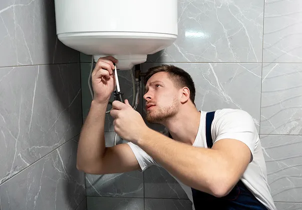 Jeune homme barbu réparant un chauffe-eau avec un tournevis.