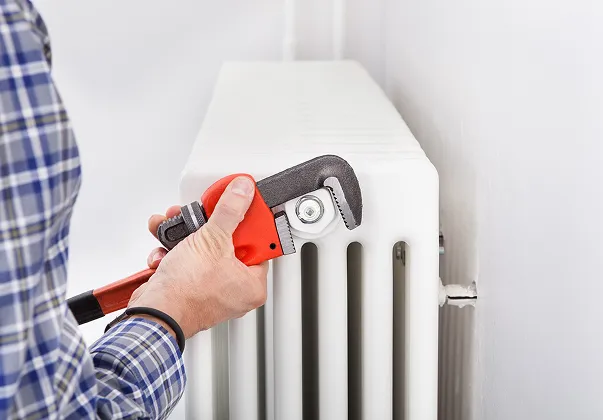 Un plombier en chemise à carreaux utilise une clé à molette sur un radiateur blanc.