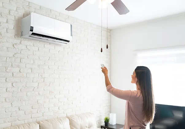 Femme ajustant la climatisation ou le ventilateur de plafond avec une télécommande.