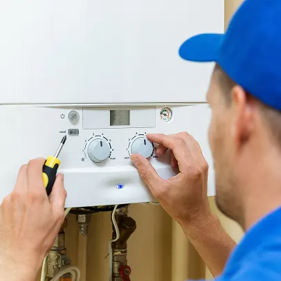 Technicien en casquette bleue ajustant les commandes d'une chaudière murale blanche à Boulogne-Billancourt en Hauts-de-Seine 92