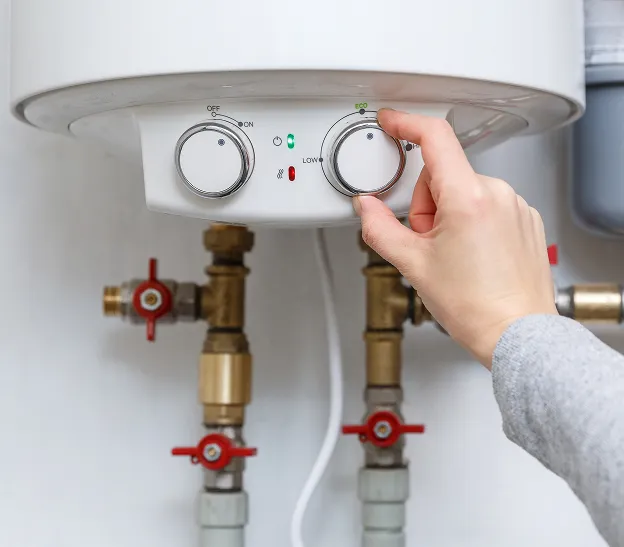 Main qui règle le thermostat d'un chauffe-eau avec des tuyaux en dessous à Boulogne-Billancourt en Hauts-de-Seine 92