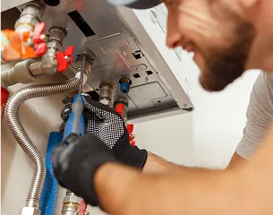 Un homme souriant, portant des gants, répare un système de chauffage central avec un tournevis à Bois-d'Arcy dans les Yvelines 78